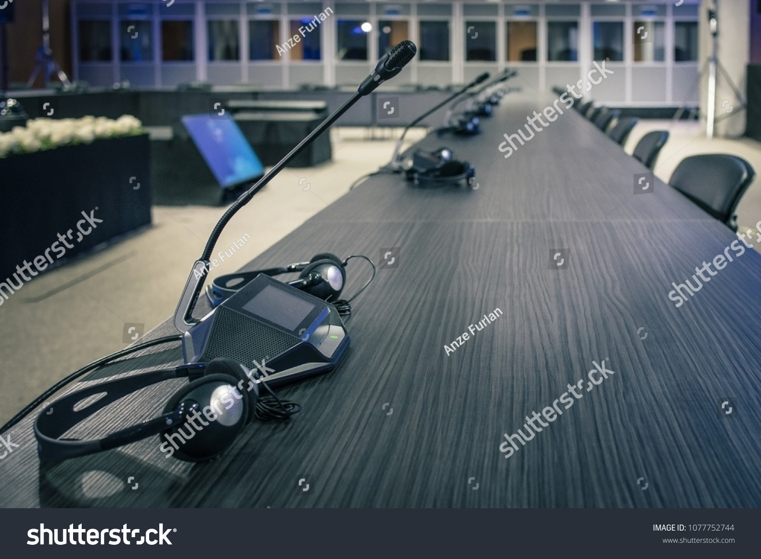 A row of microphone and headphone sets for speech and translation on a business or congress meeting on a desk. Translation booths are seen in the background. #1077752744