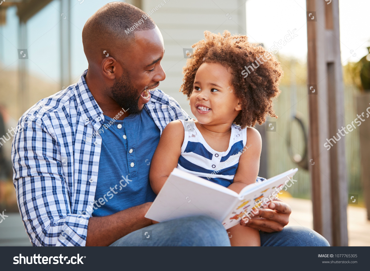 Young black father and daughter reading book outside #1077765305