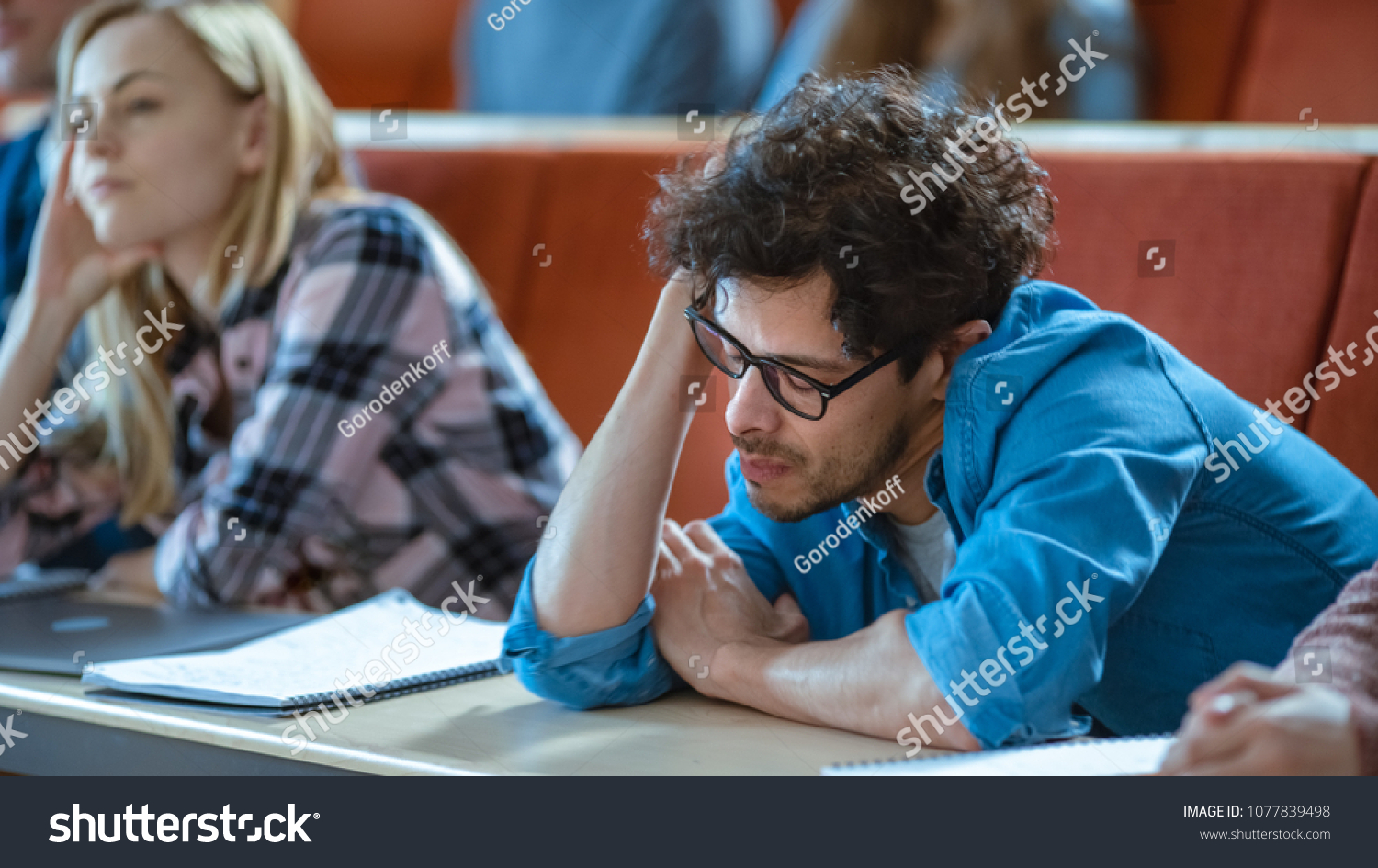 Bored Male Student Listens Lecture at the University. Tired, Exhausted and Overworked Young Male Holds His Head. #1077839498