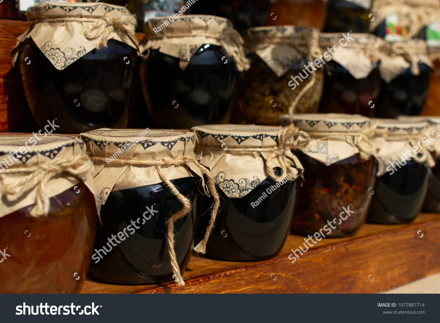 Shelves with composed handmade jam conserved in glass jars and decorated with strings. #1077887714
