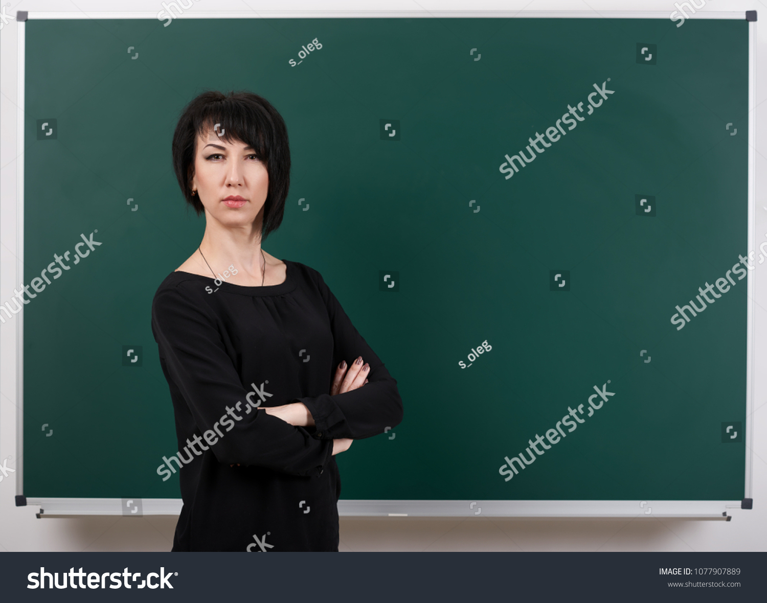 strict teacher posing by chalk Board, learning concept, green background, Studio shot #1077907889