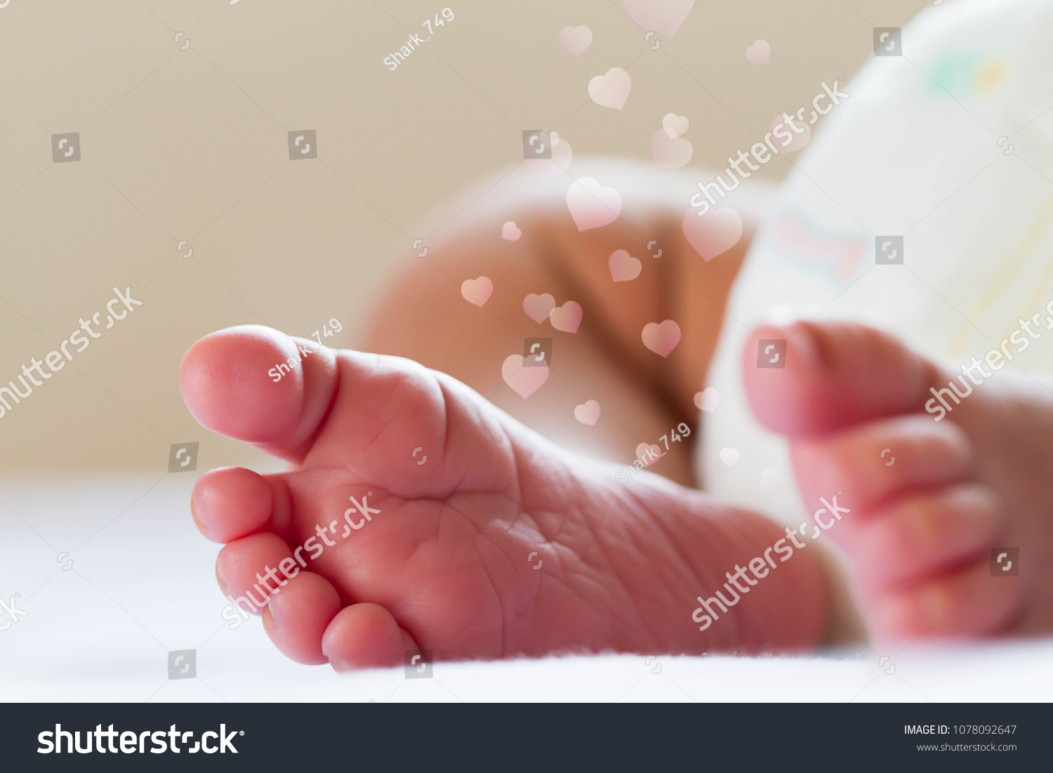 Newborn baby infant feet on white bed with floating hearts #1078092647