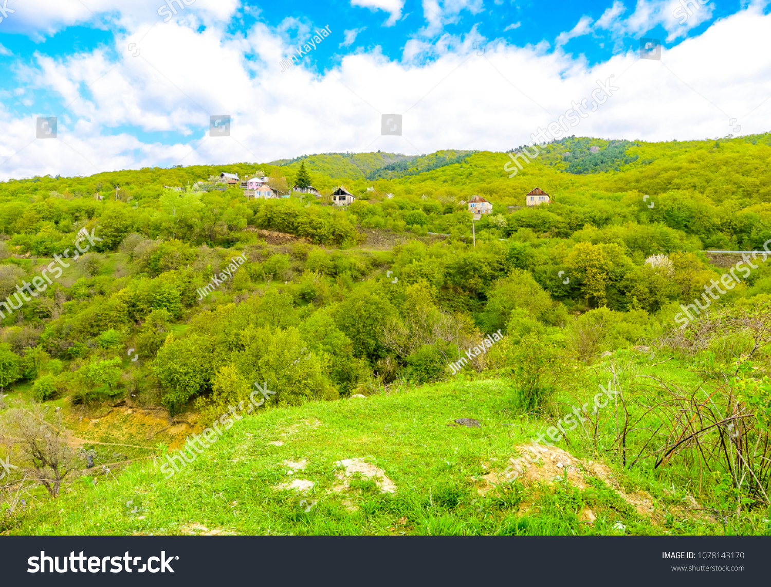 Beautiful pristine mountain village nestled against mountains and spring greens with blue skies and puffy clouds. #1078143170