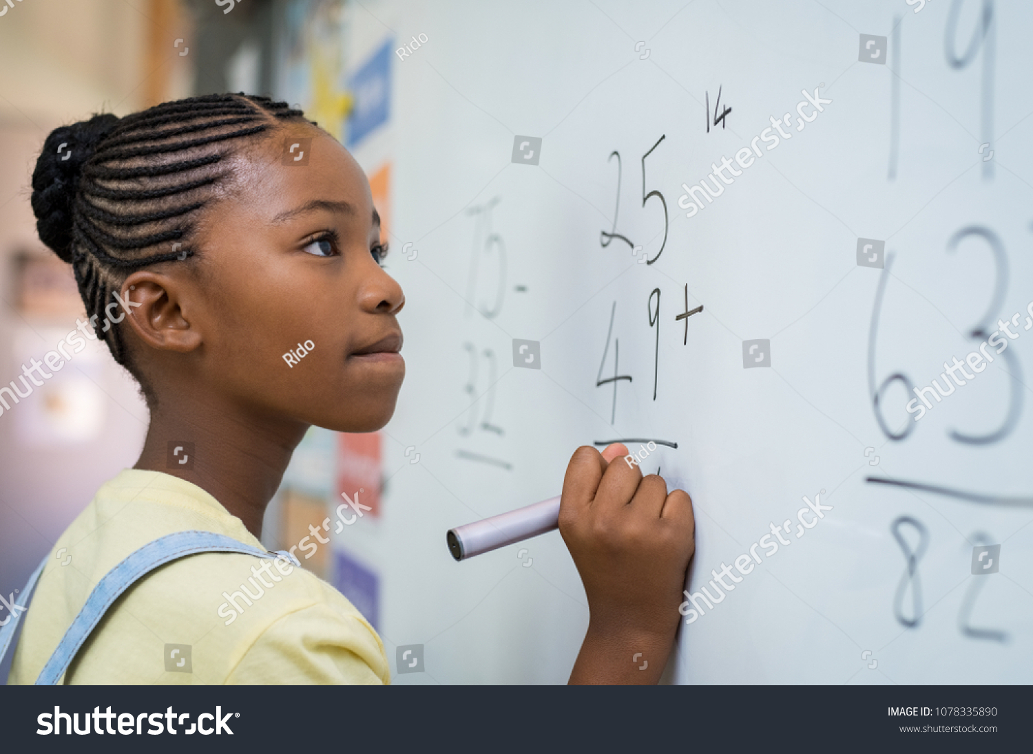 Portrait of african girl writing solution of sums on white board at school. Black schoolgirl solving addition sum on white board with marker pen. School child thinking while doing mathematics problem. #1078335890