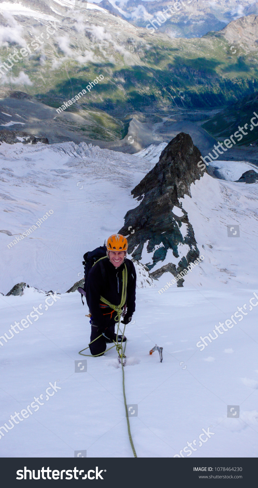 male mountain climber on a high alpine glacier with a great view of the fantastic mountain landscape behind him #1078464230