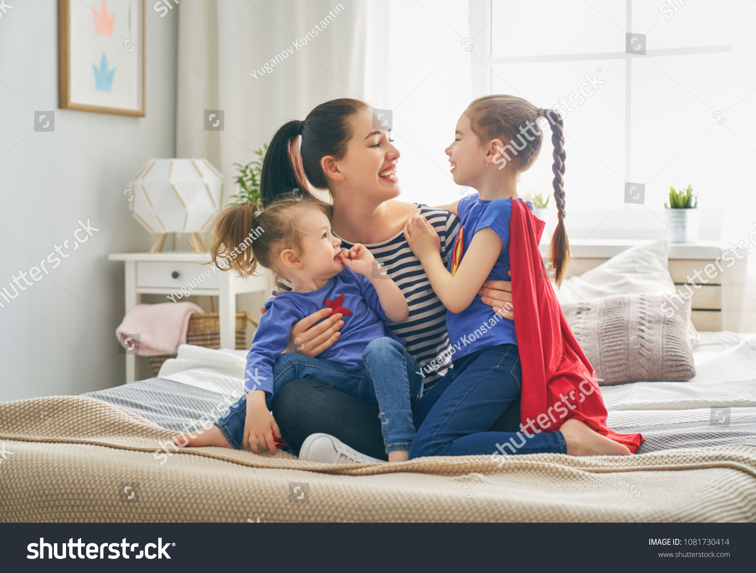Mother and her children playing together. Mom and girls in Superhero costumes. Mum and kids having fun, smiling and hugging. Family holiday and togetherness. #1081730414