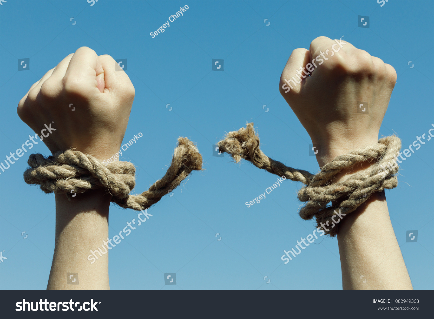 Hands tearing shackles the background of blue sky. Concept of freedom #1082949368