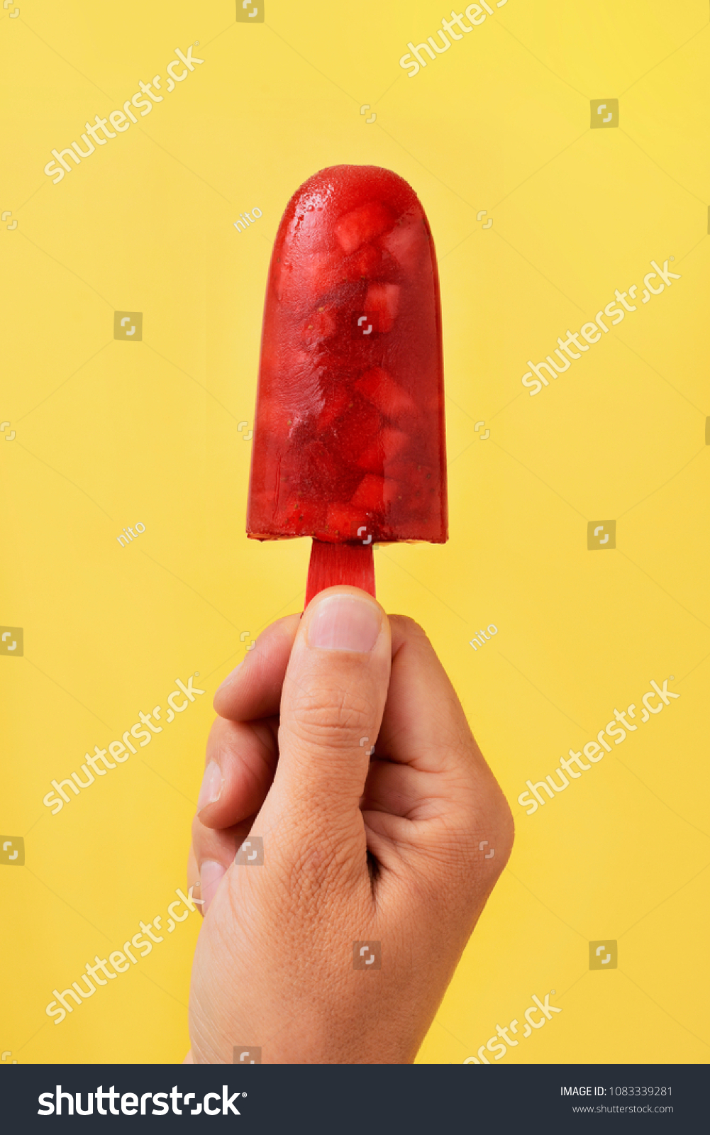 closeup of a young caucasian man with a homemade natural ice pop in his hand, against a yellow background #1083339281