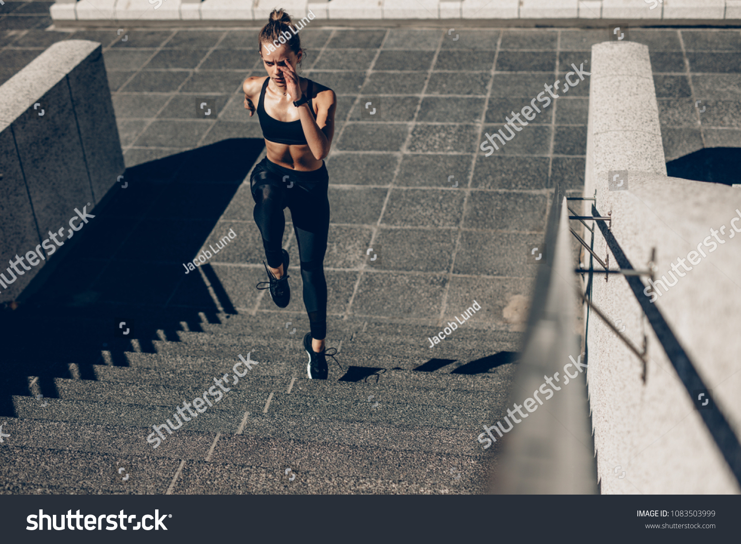 Fit sportswoman running up the steps. Female runner exercising on staircase outdoors. #1083503999