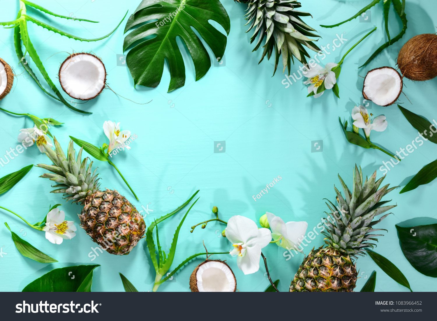 Summer tropical background with a space for a text, various fruits, green leaves and flowers arranged in a way that light shadows are fallen on the background surface, helping to keep some sum #1083966452