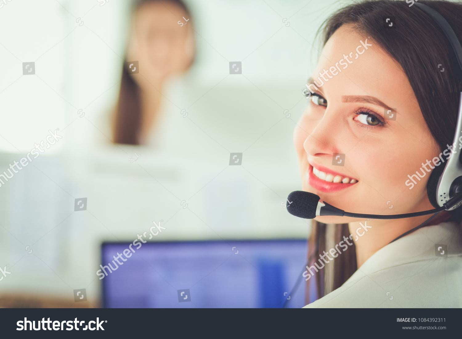 Smiling businesswoman or helpline operator with headset and computer at office #1084392311