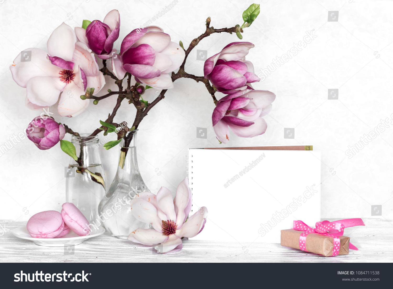 Creative layout made with pink magnolia flowers, empty card, macarons and gift box on white wooden background. mock up. still life. wedding frame. spring minimal concept #1084711538