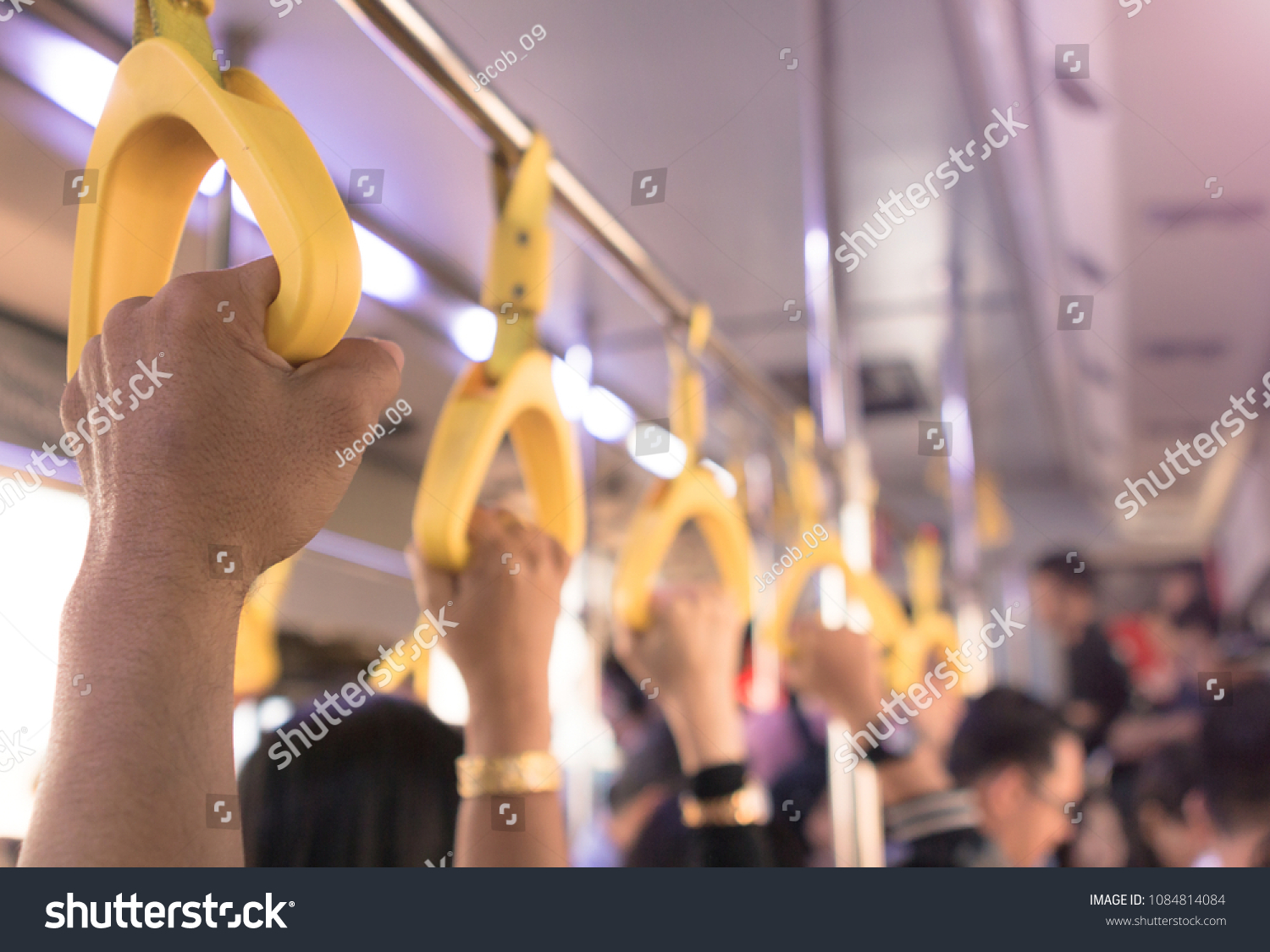 People hand holding yellow handle on the bus  with a large crowd #1084814084