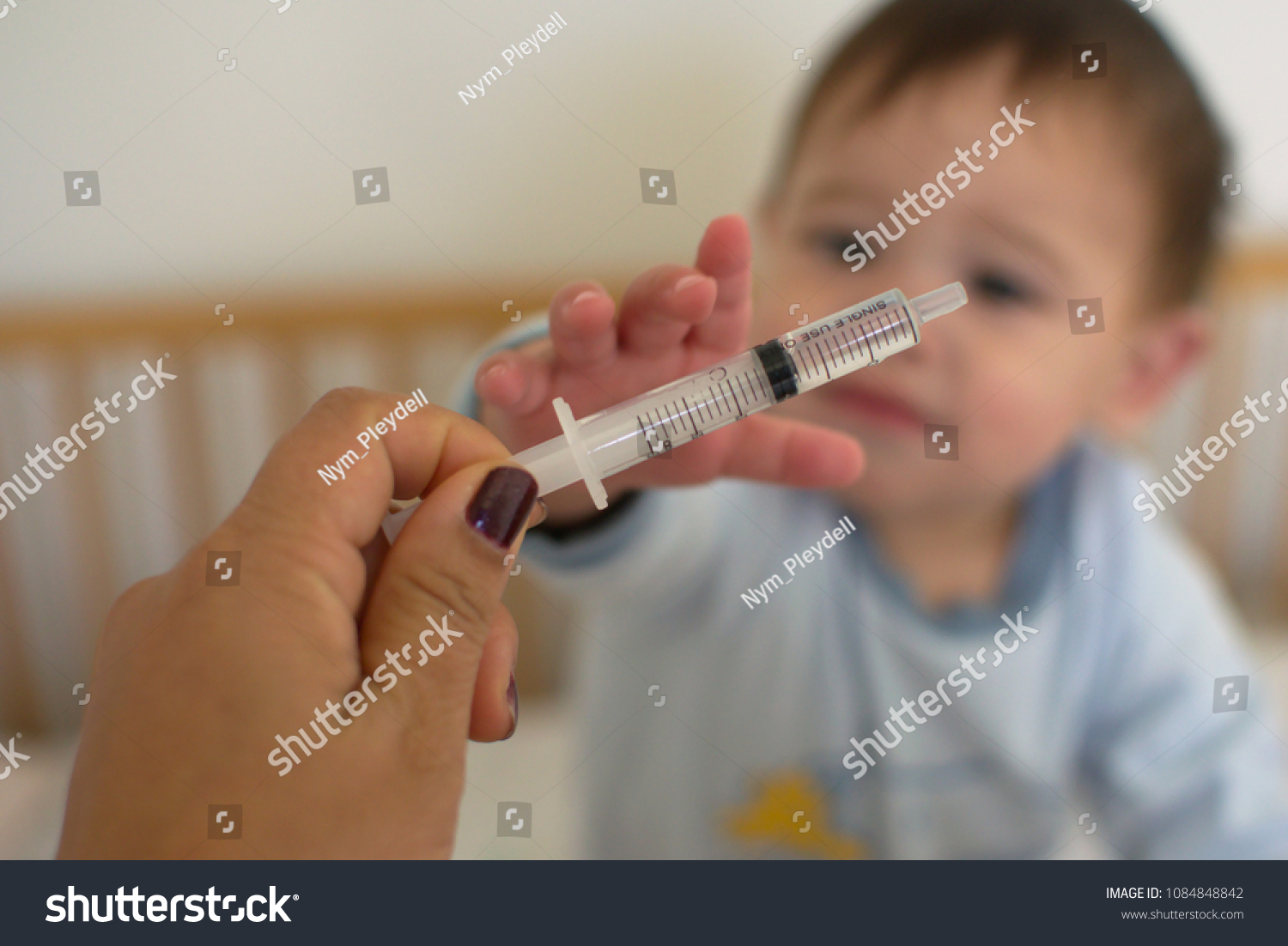 Mother offer the oral liquid medicine in syringe to the blurred baby in the background   #1084848842