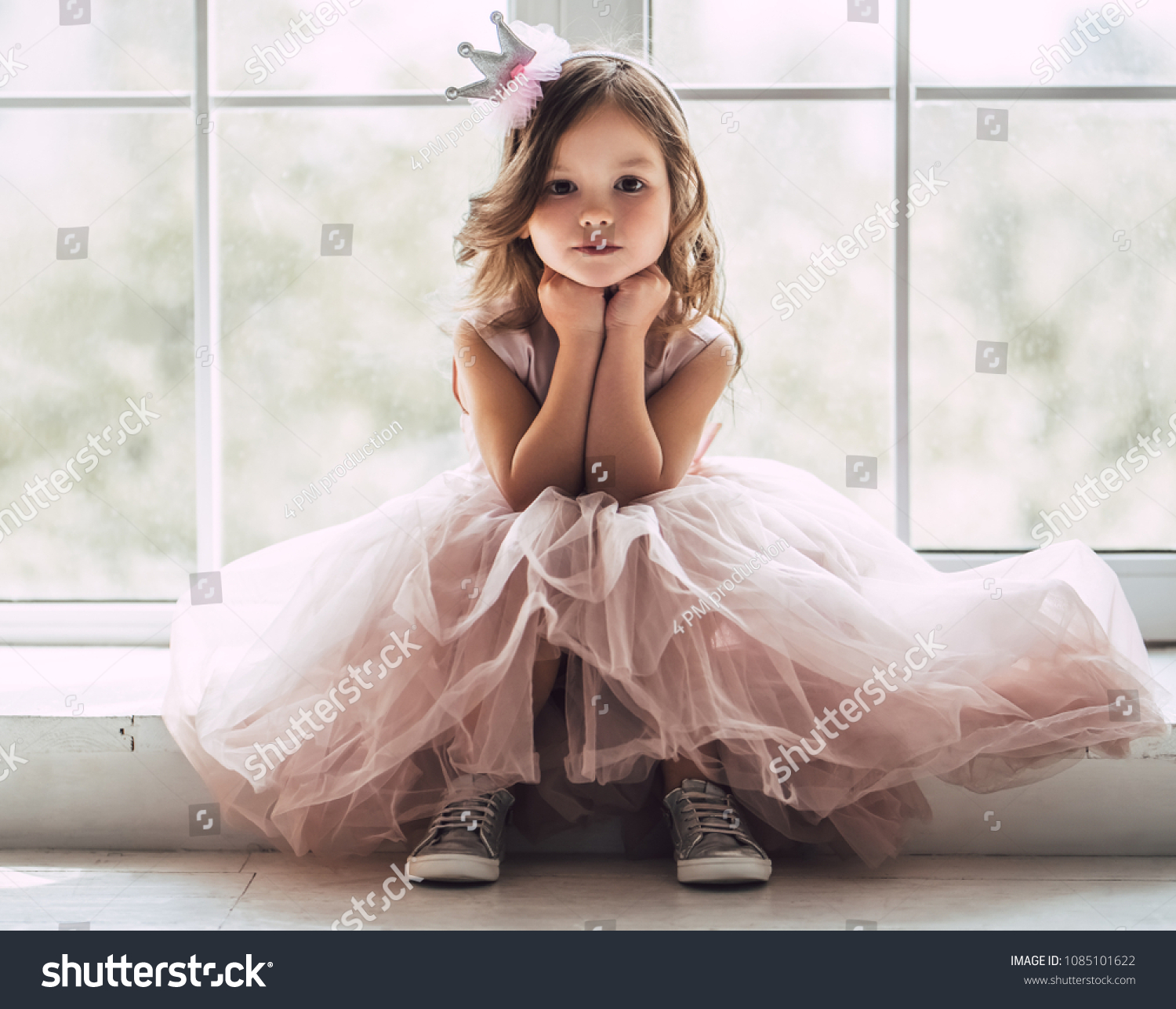 Little cute girl in beautiful dress is sitting near the window at home. #1085101622