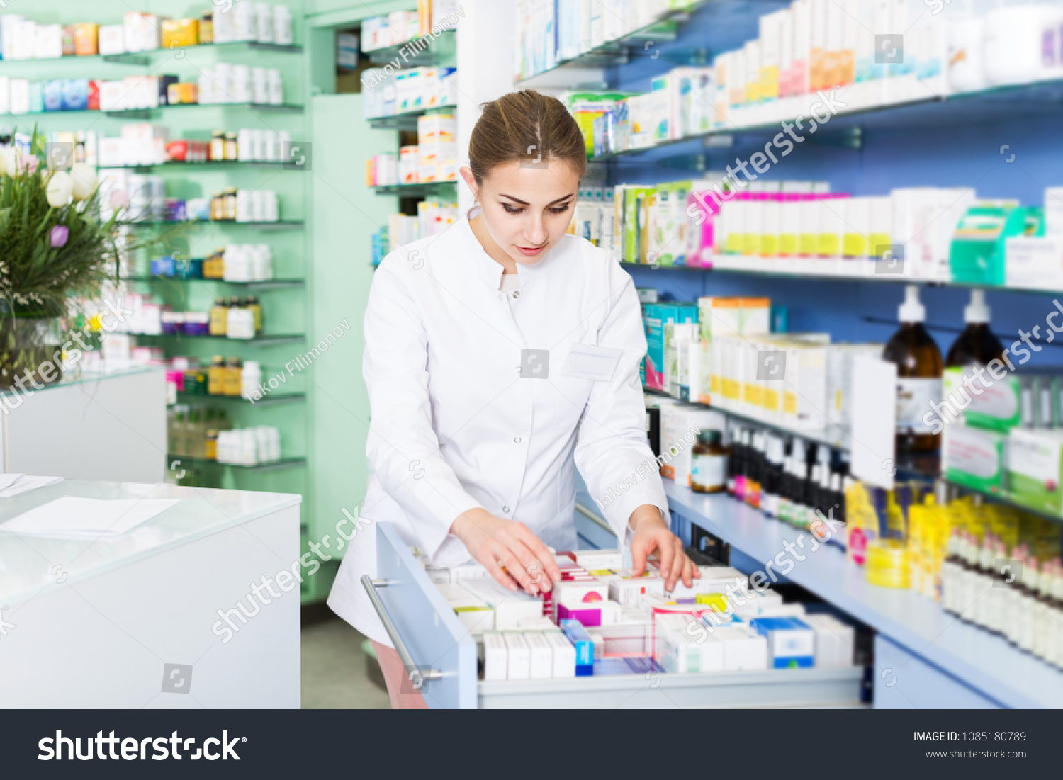 Woman specialist is attentively looking medicines in lockers in pharmacy #1085180789