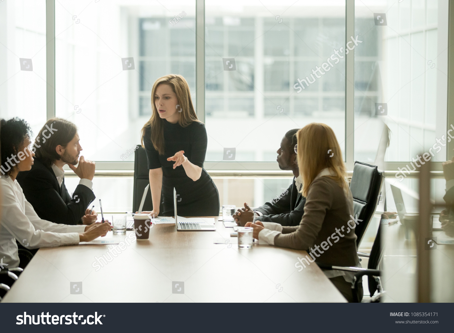 Serious woman boss scolding employees for bad results or discussing important instructions at multiracial team meeting, dissatisfied female executive talking to multiracial team at boardroom briefing #1085354171