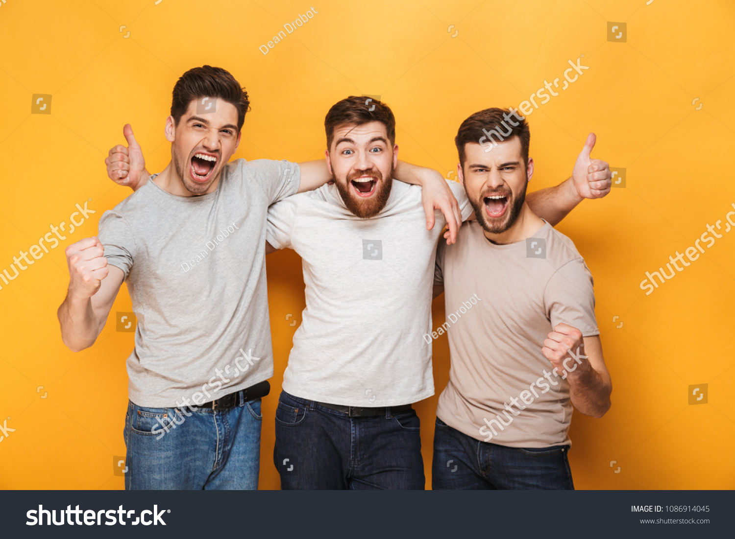 Three young excited men showing thumbs up and celebrating isolated over yellow background #1086914045