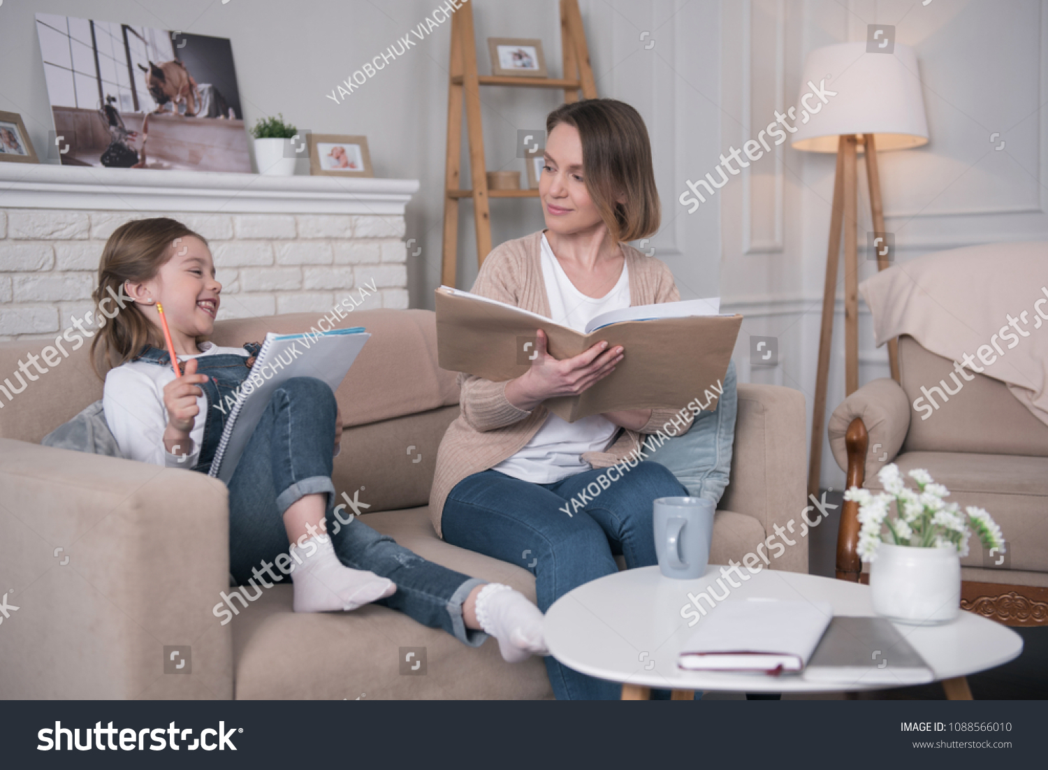 Wonderful day. Adorable glad girl sitting on the couch with her mother and studying #1088566010