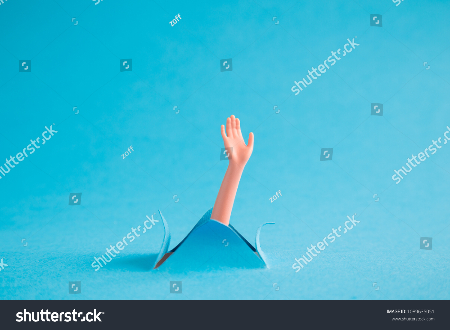 Doll arm emerging from blue paper background. Drowning minimal creative abstract concept. #1089635051