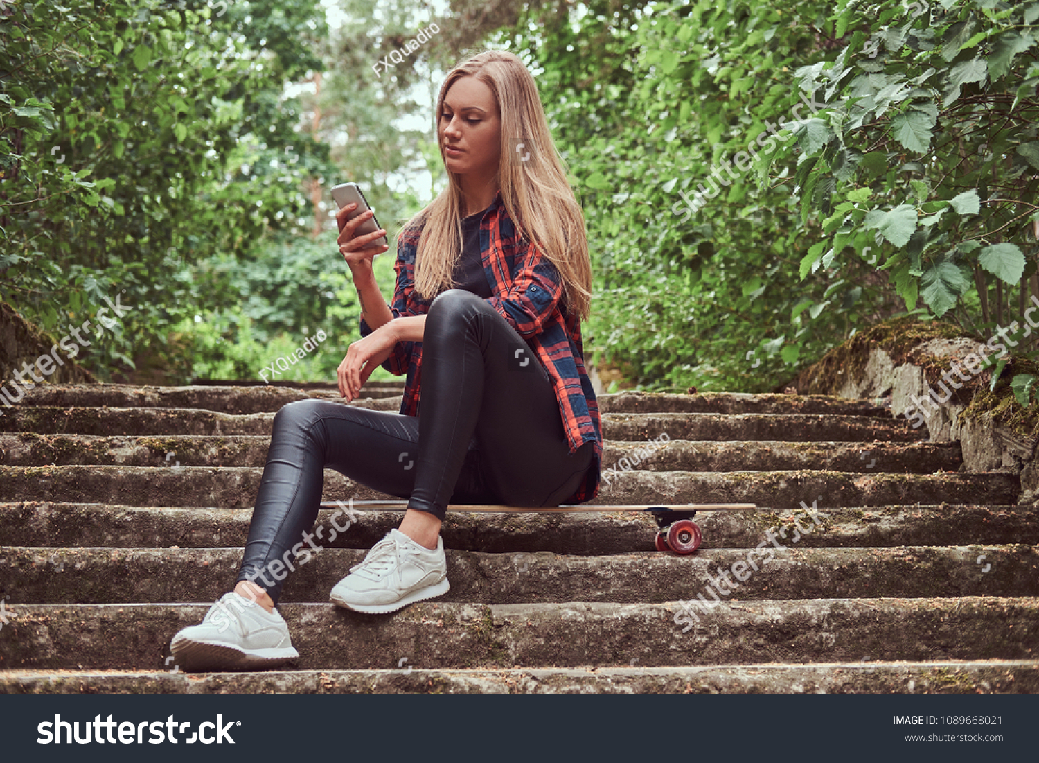 Young blonde hipster girl using a smartphone while sitting on steps in a park. #1089668021