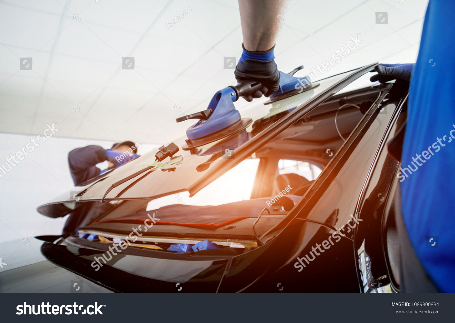 Automobile special workers replacing windscreen or windshield of a car in auto service station garage. Background #1089800834