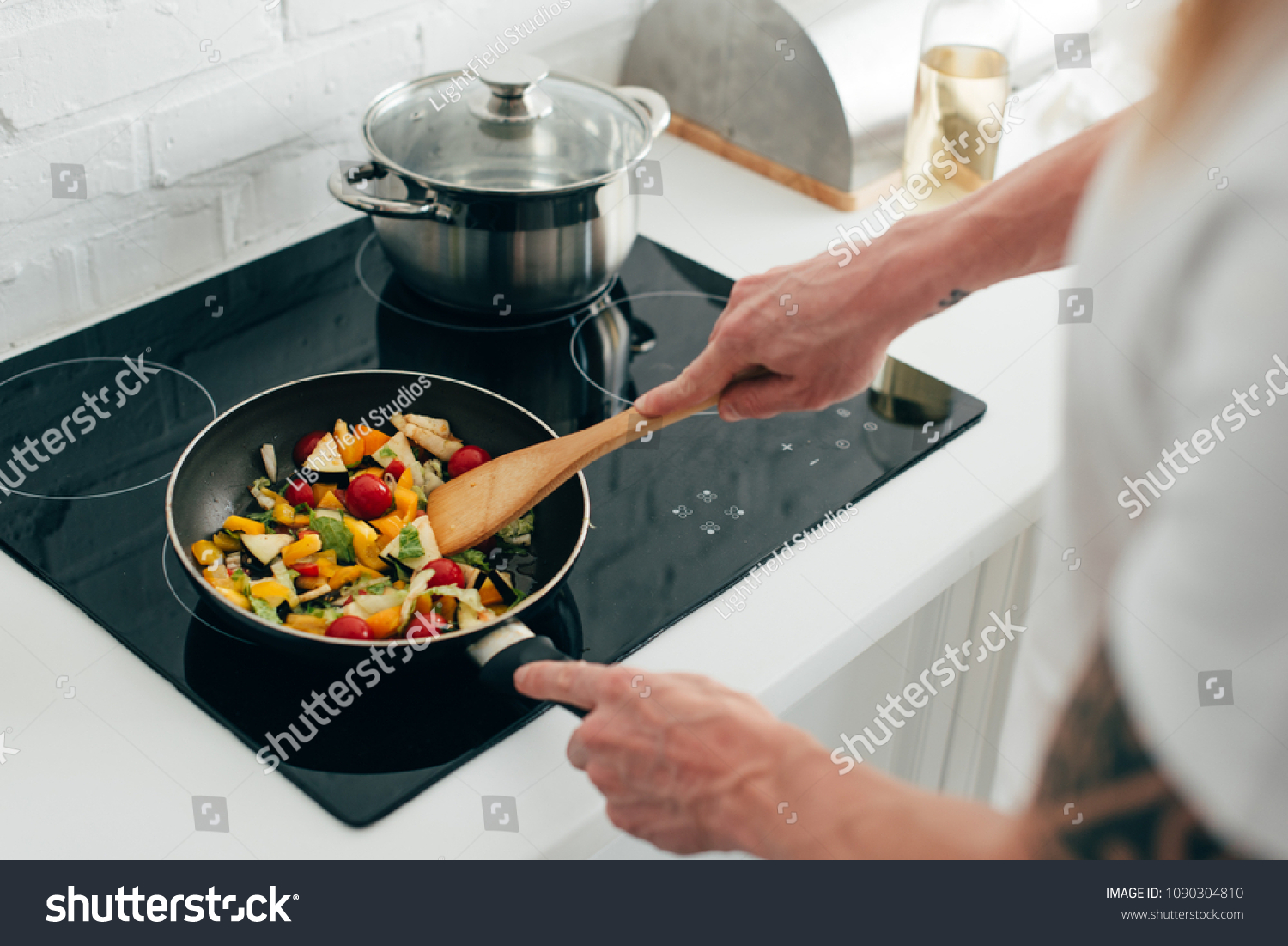 cropped shot of man cooking vegetables in frying pan on electric stove #1090304810