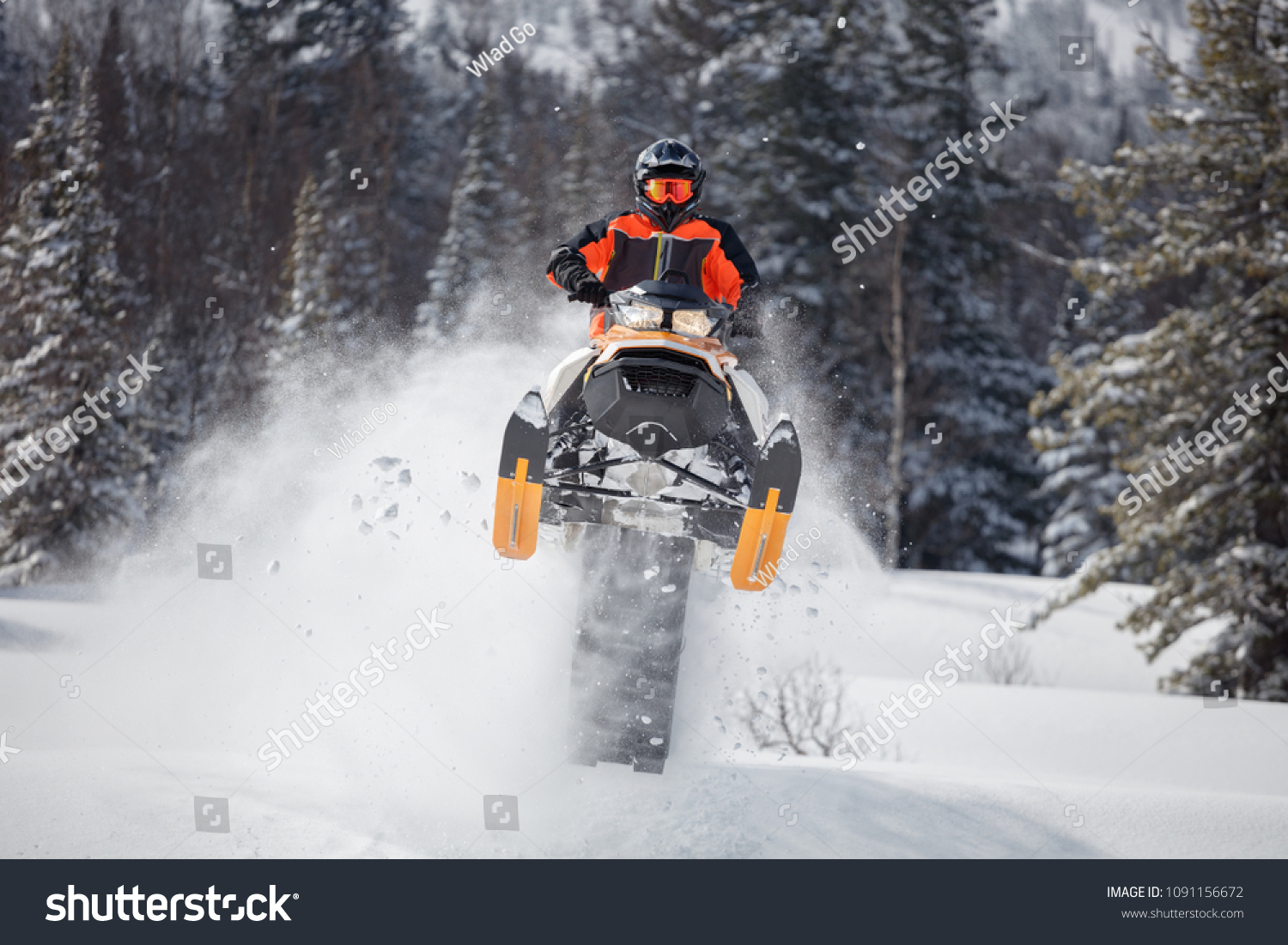 the guy is flying and jumping on a snowmobile on a background of winter forest  leaving a trail of splashes of white snow. bright snowmobile and suit without brands. extra high quality #1091156672