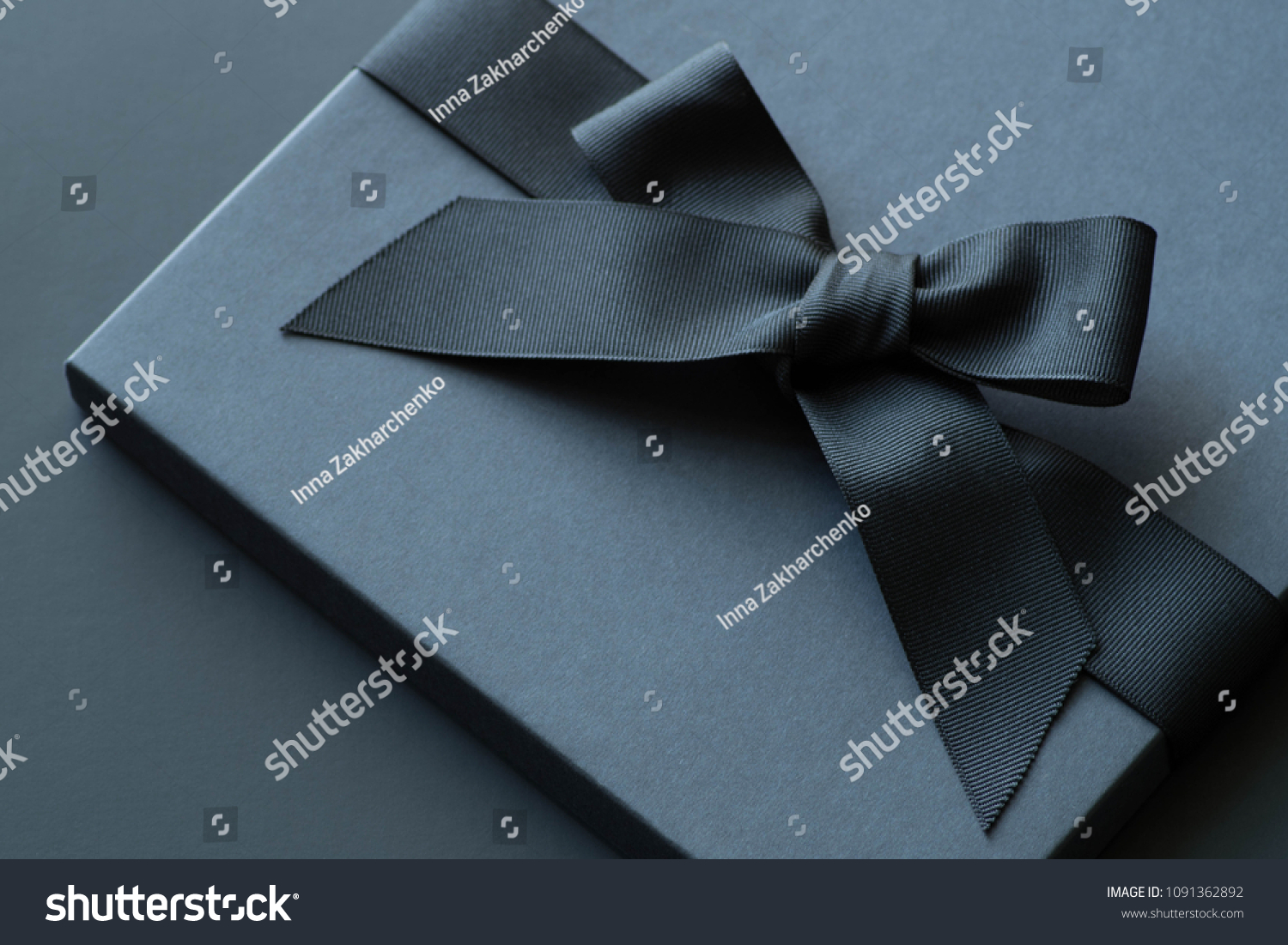 Black gift box on a dark contrasted background, decorated with a textured bow and feathers, creating a romantic atmosphere. Typically used for birthday, anniversary presents, gift cards, post cards. #1091362892