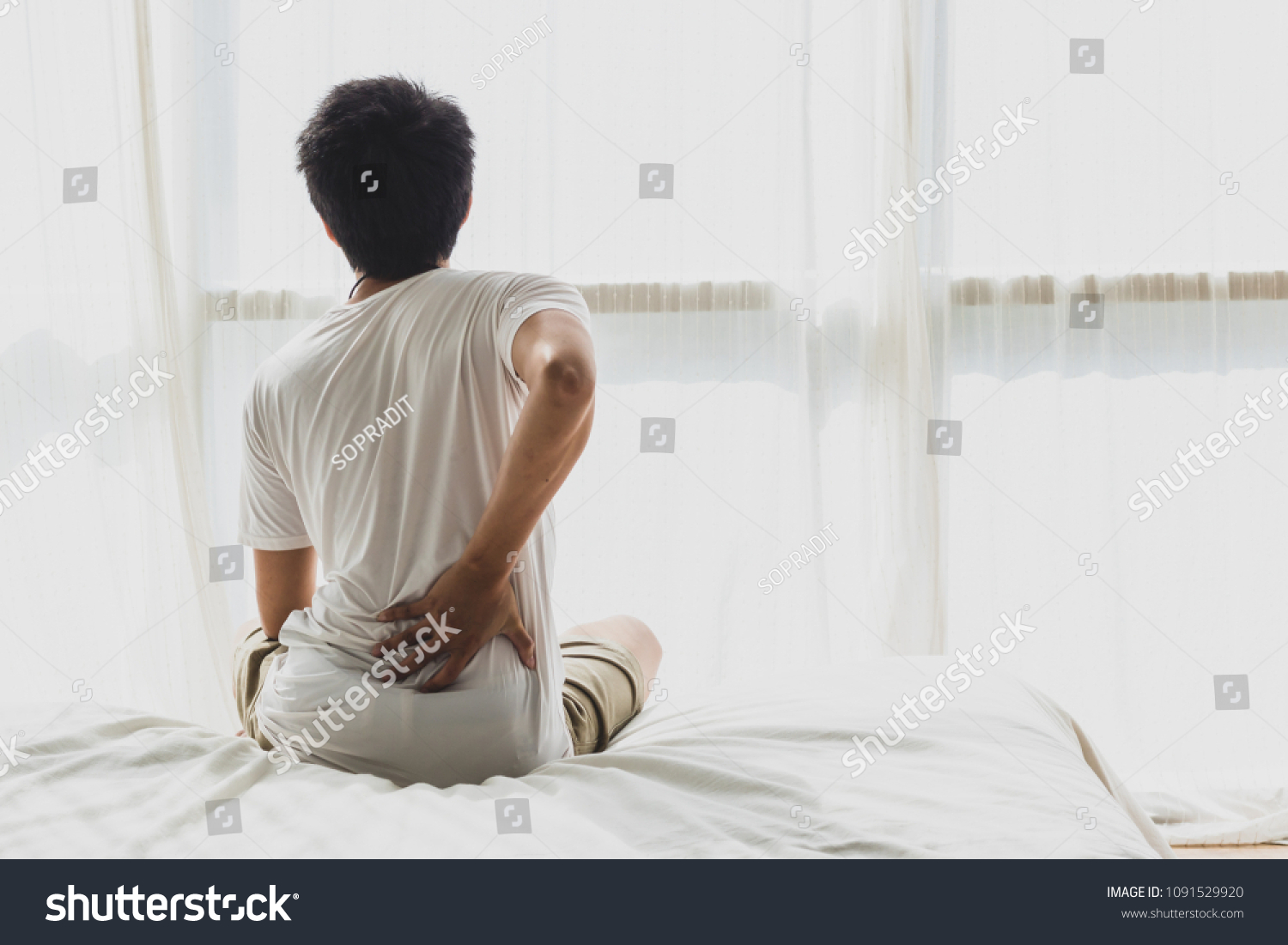 Asian man back pain and sit on bed in bedroom in the morning.color tone #1091529920