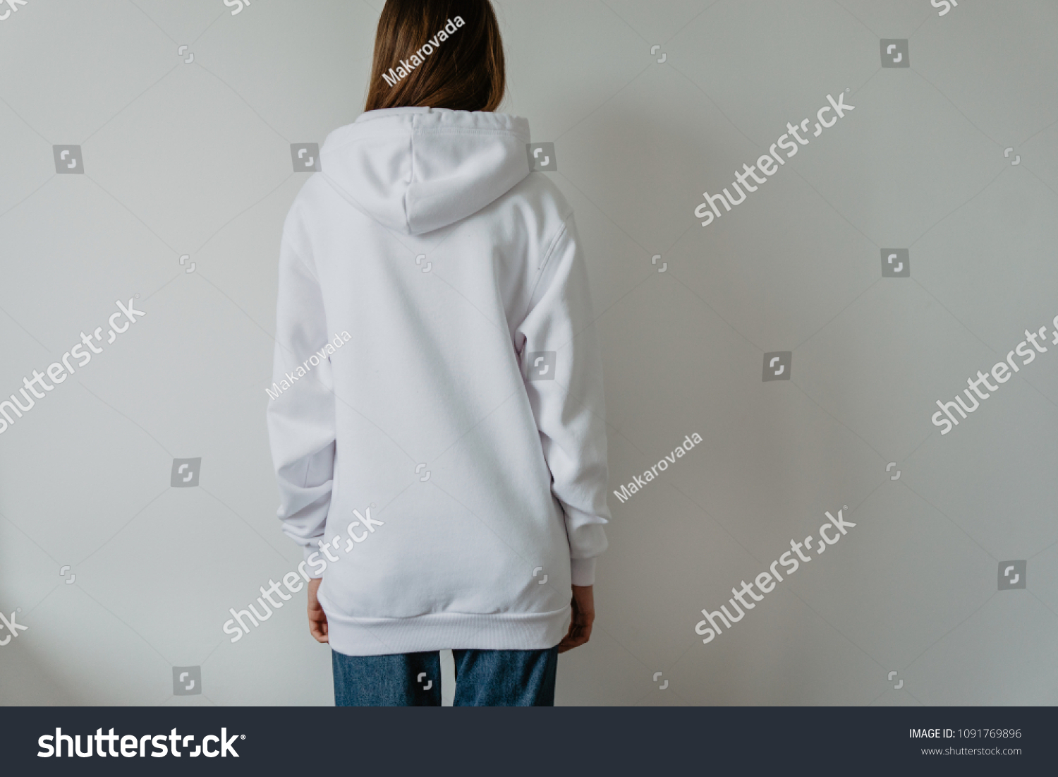 Pretty young fit girl wearing blank white hoodie with copy space for your logo or design, mock-up of template sweatshirt, white wall in the background, back view #1091769896