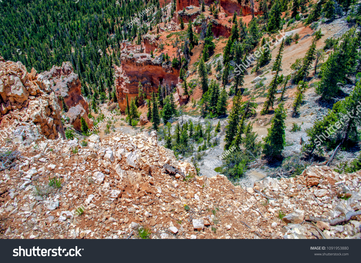 Looking over a cliff down into a valley with green trees and red sandstone formations. #1091953880