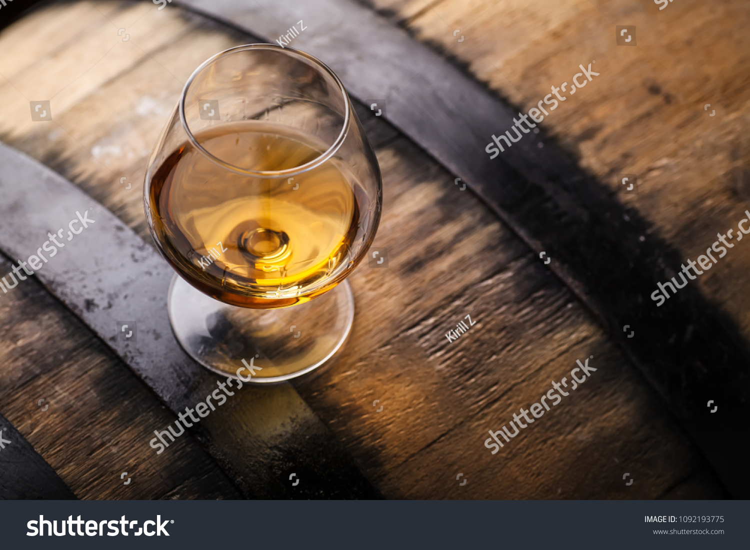 Snifter glass of brandy standing on an oak barrel in a cellar #1092193775