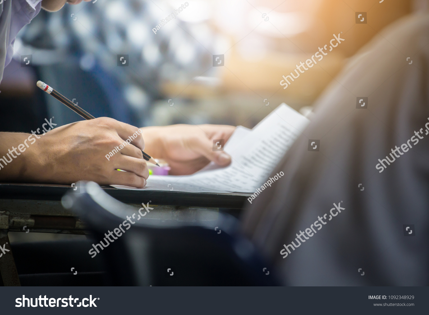 soft focus.hand high school or university student in uniform holding pencil writing on paper answer sheet.sitting on lecture chair taking final exam or study attending in examination room or classroom #1092348929
