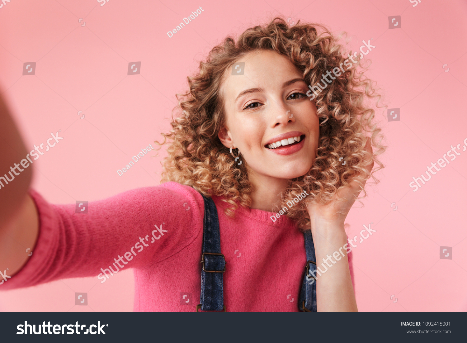 Portrait of happy young girl with curly hair taking a selfie isolated over pink background #1092415001