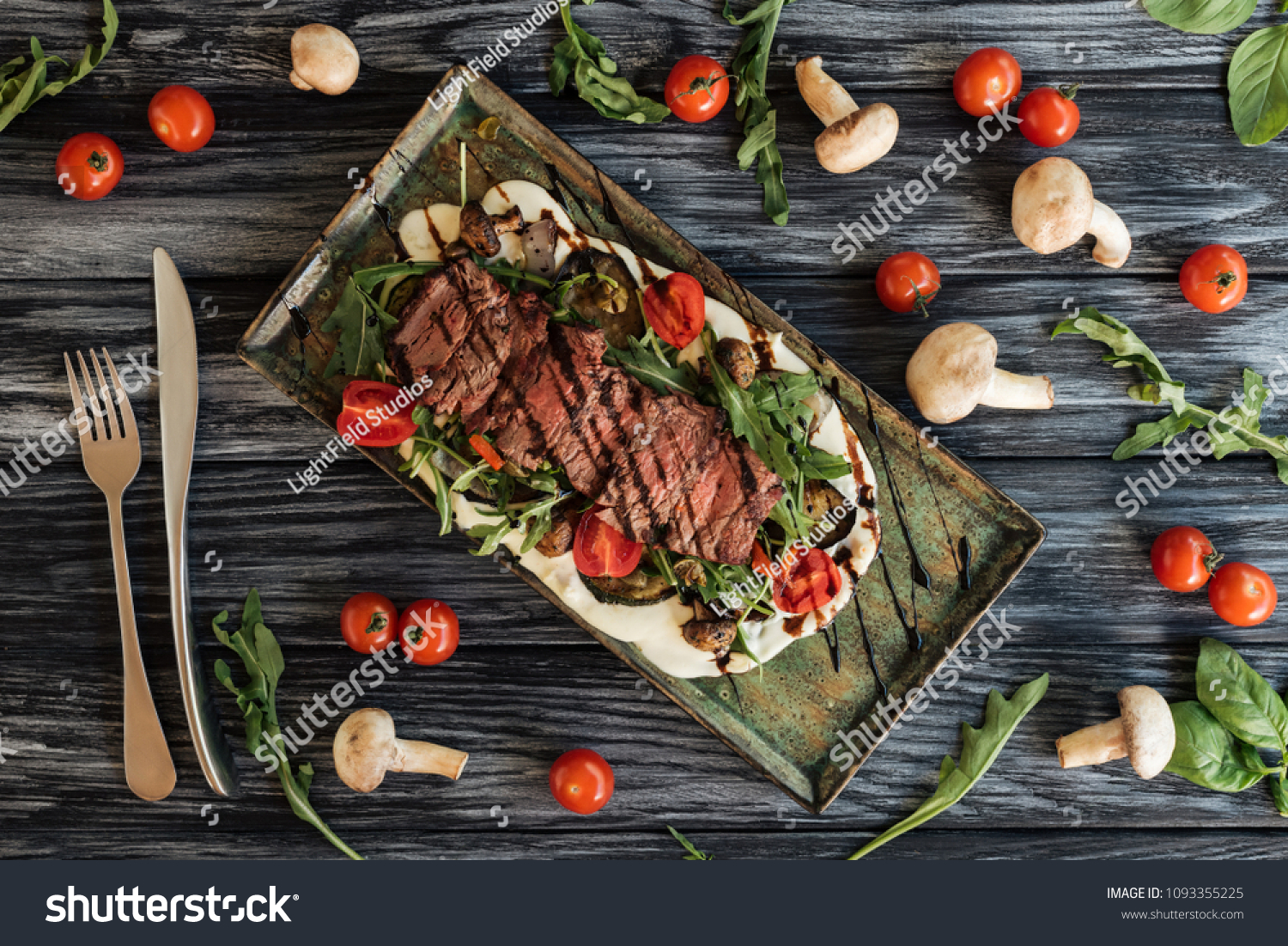 top view of delicious roasted steak, fork with knife and vegetables on wooden table  #1093355225
