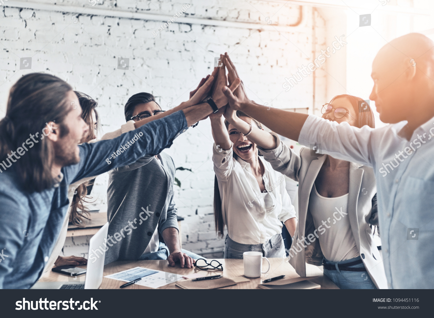 High-five for success! Diverse group of business colleagues giving each other high-five in a symbol of unity and smiling while working in the board room #1094451116