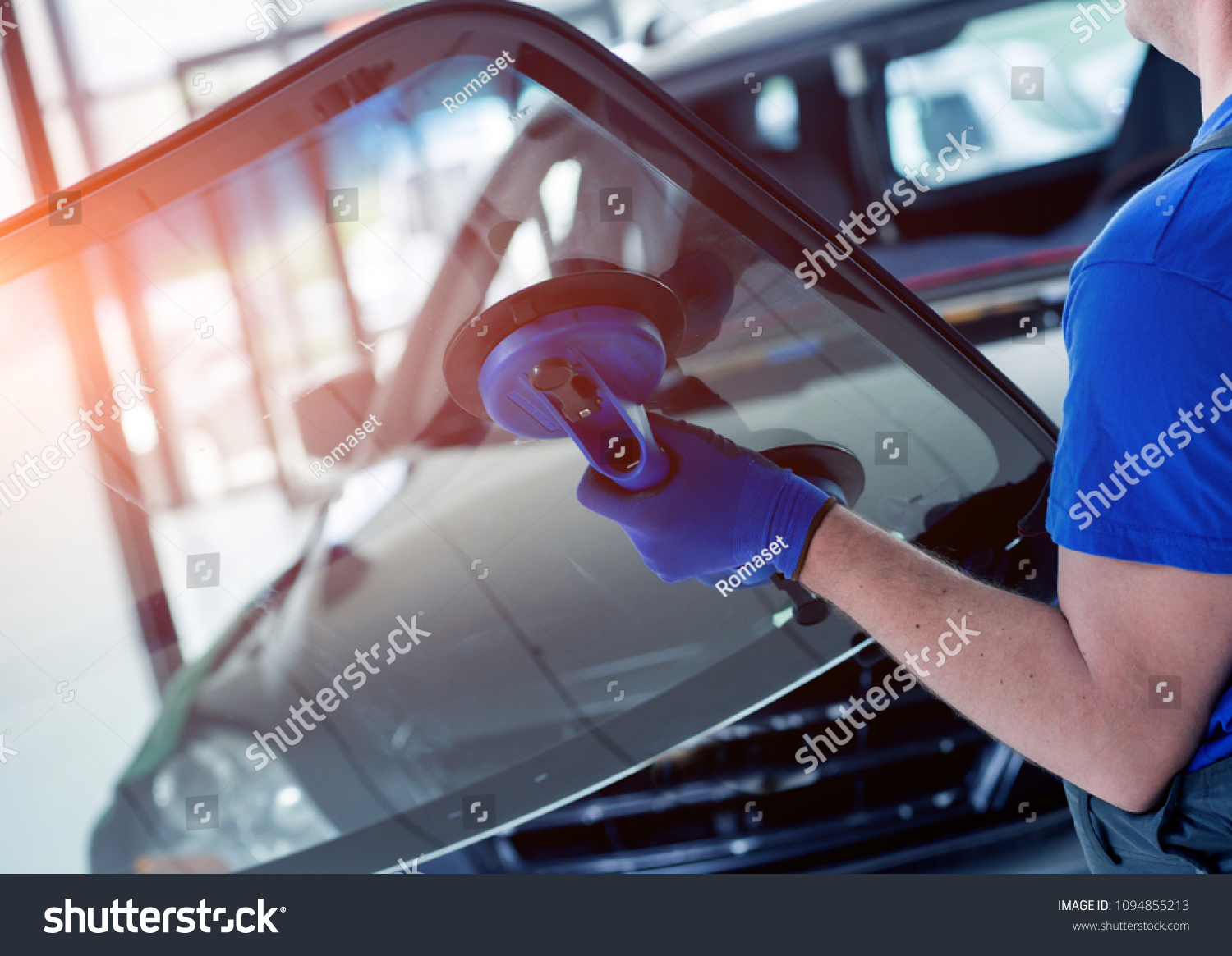 Automobile special workers replacing windscreen or windshield of a car in auto service station garage. Background #1094855213