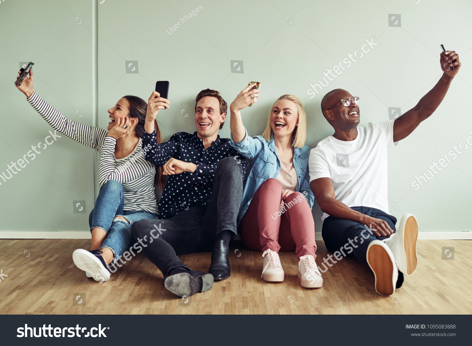 Group of diverse young businesspeople sitting on an office floor taking selfies together while on their break #1095083888