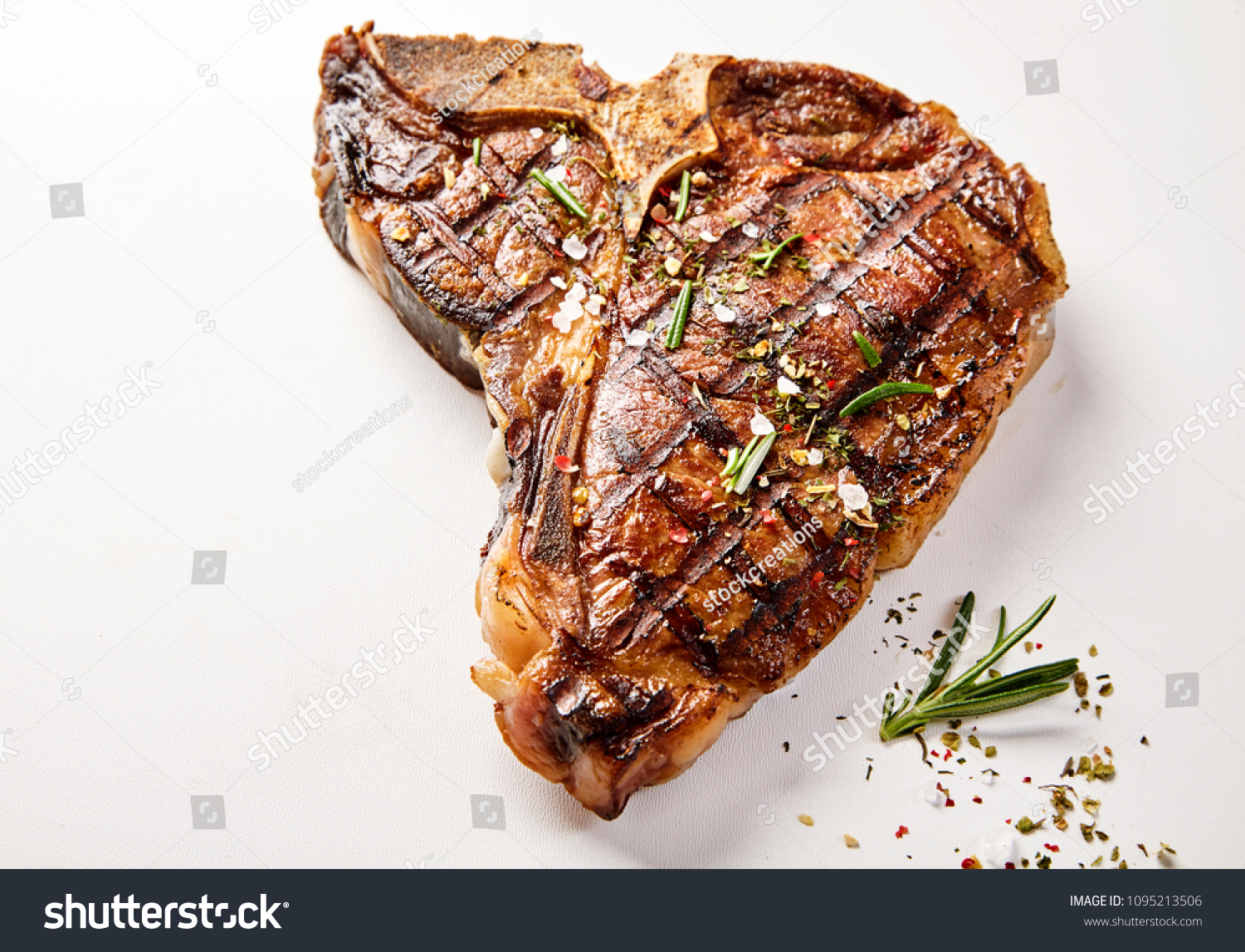 A succulent, grilled t-bone steak and herb garnish with a white background and copy space. #1095213506