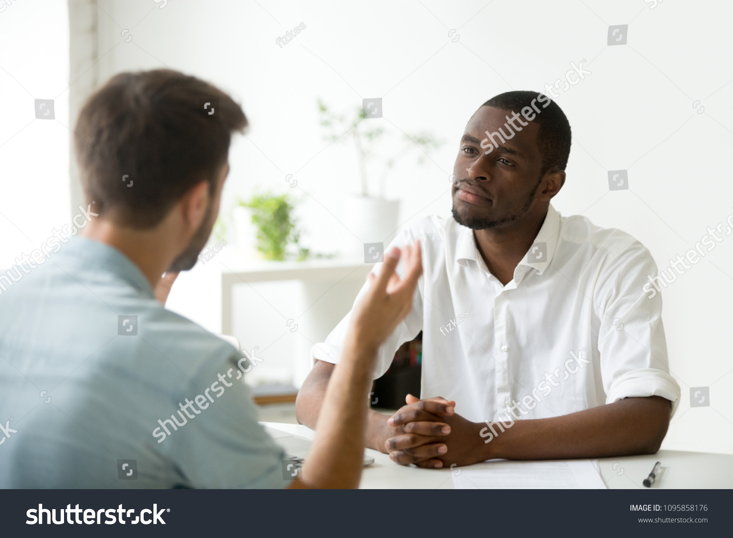 African American employer listening attentively to caucasian job applicant talking at work interview, being friendly and interested to candidate. Concept of recruiting, employment, hiring #1095858176