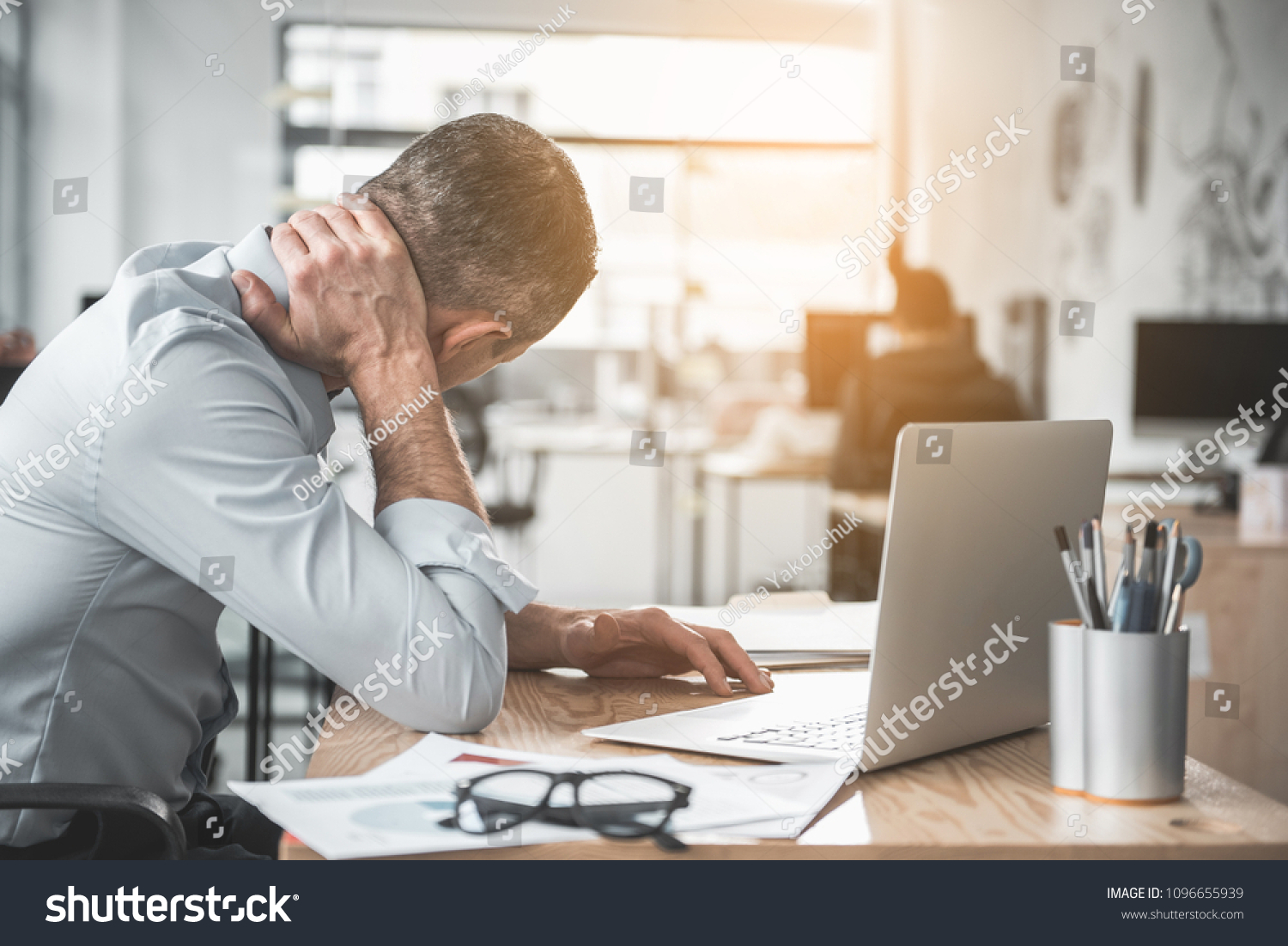Man holding sore neck while using notebook computer. He sitting at table. Sick worker concept #1096655939