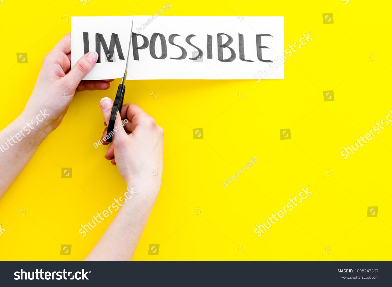 All is possible concept. Hands cutting the part im of written word impossible by sciccors. Yellow background top view copy space #1098247367