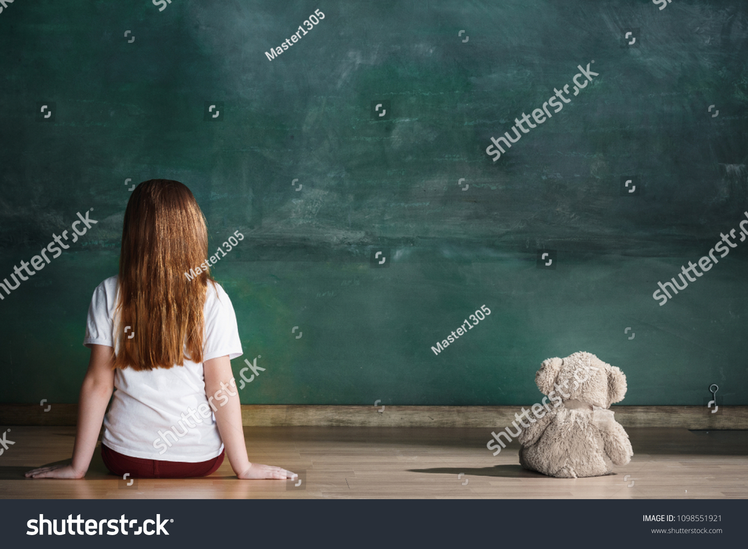 Little autistic girl with teddy bear sitting on floor at empty room. Autism concept. Conceptual image with little caucasian model at studio. Back view #1098551921