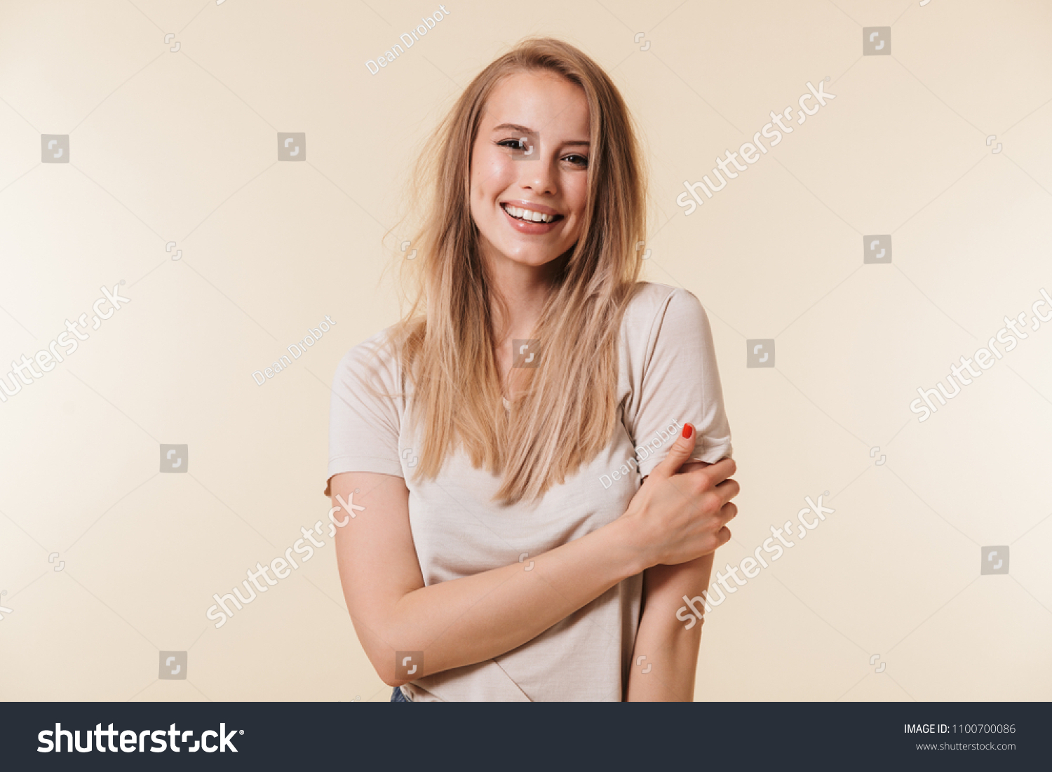 Portrait of beautiful woman 20s with blond hair in basic t-shirt smiling and looking at camera isolated over beige background in studio #1100700086