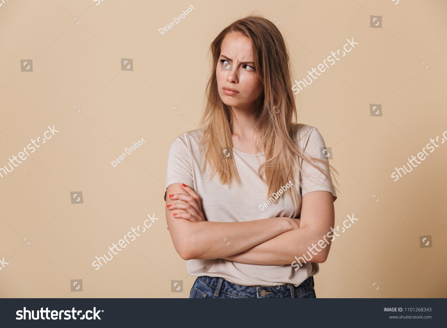 Portrait of an upset casual girl with arms folded looking away isolated over beige background #1101268343