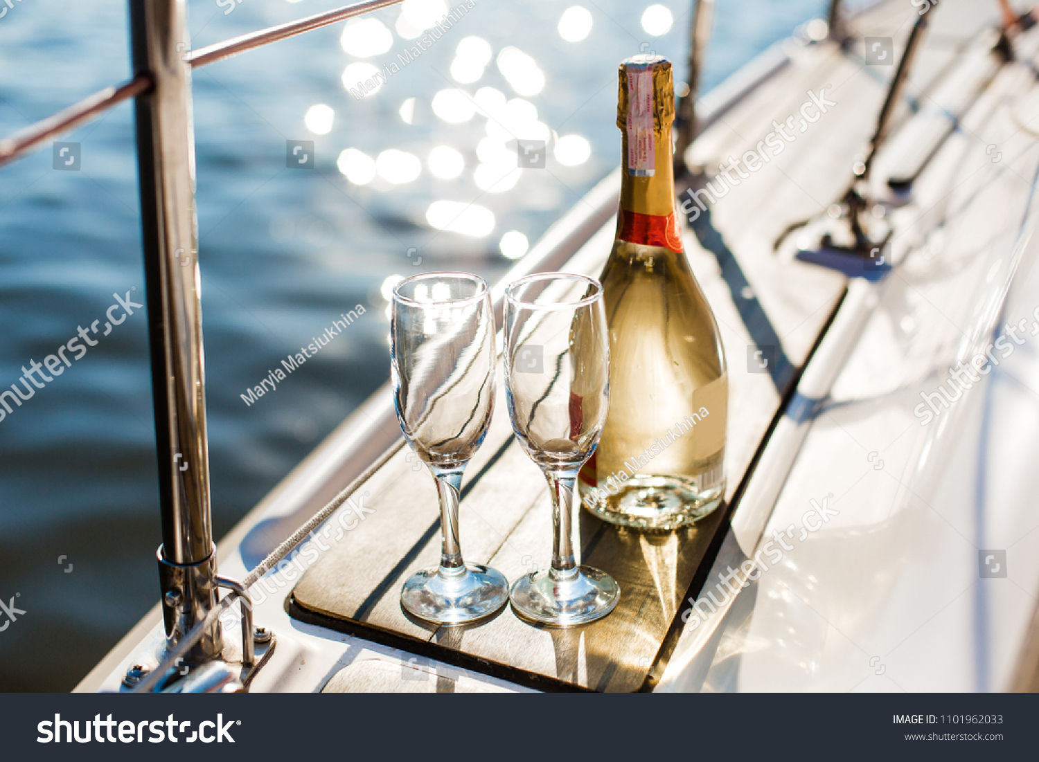 Romantic luxury evening on cruise yacht with champagne setting. Empty glasses and bottle with champagne and tropical sunset with sea background, nobody. #1101962033
