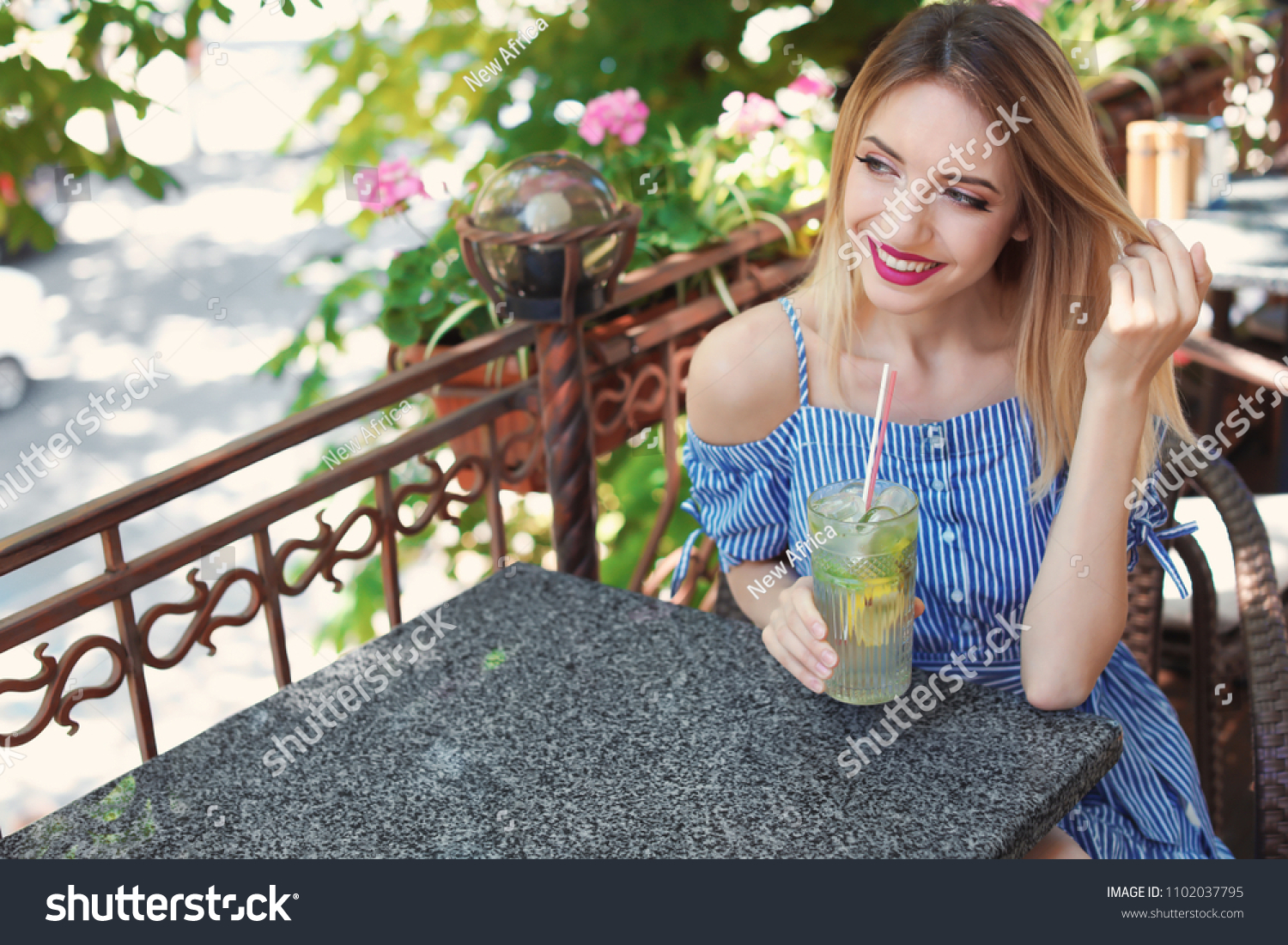 Young woman with glass of tasty lemonade at table in cafe, outdoors. Natural detox drink #1102037795