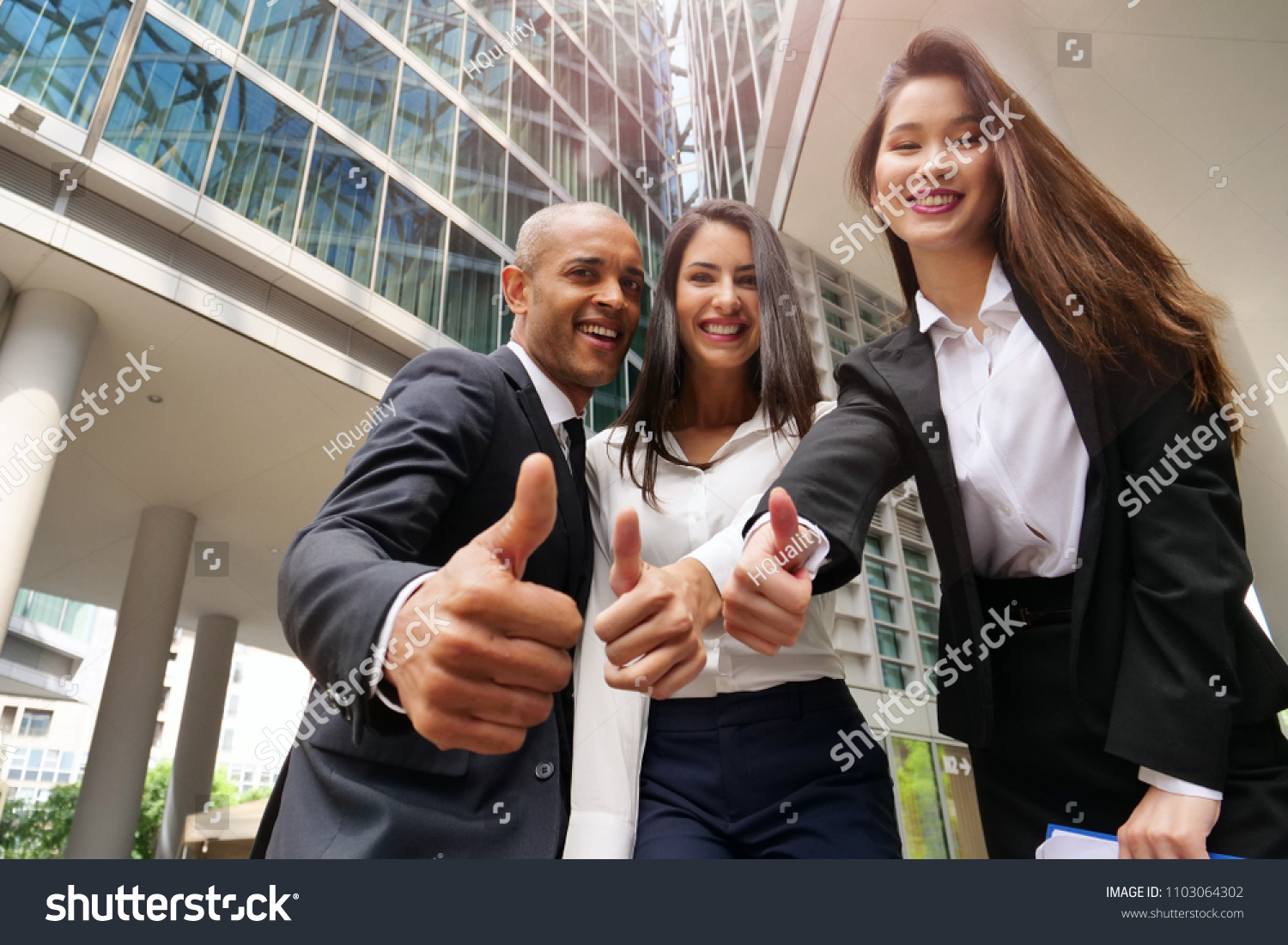 Business people of different ethnicities dressed in suits and ties, smile and "ok" raising their thumbs to celebrate the team's success. Concept of: internationality and career, cooperation. #1103064302