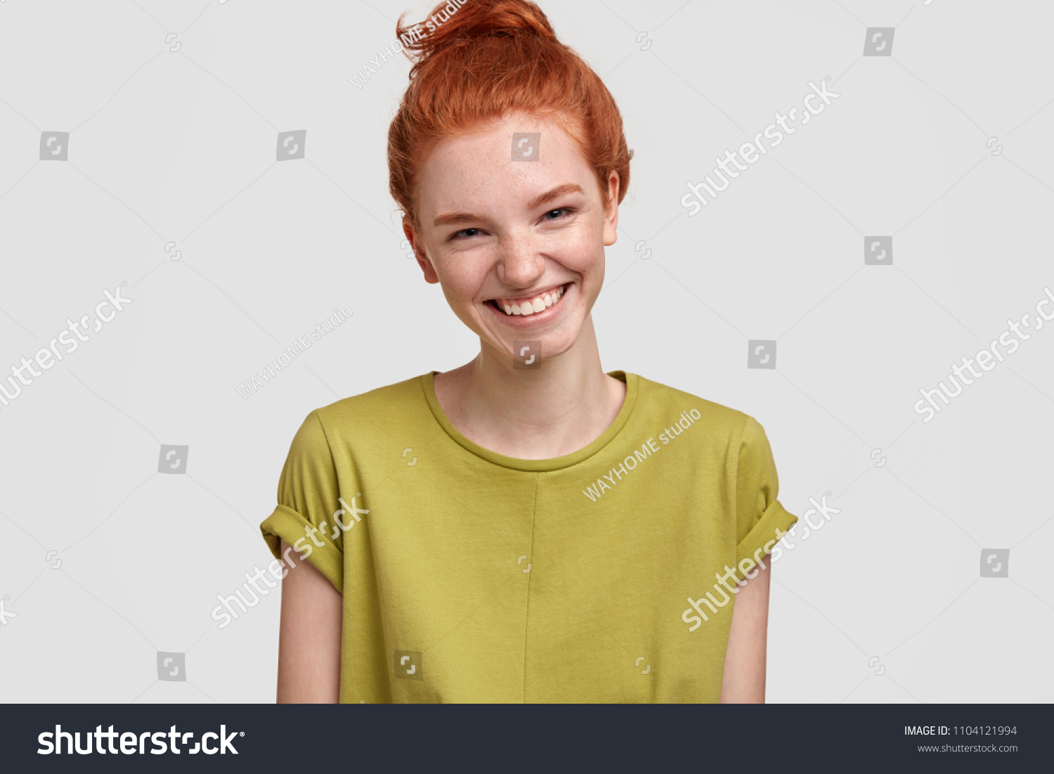 Indoor shot of beautiful young female with freckled skin, laughs at funny joke, smiles positively, watches hilarious show or comedy, dressed in green casual t shirt, isolated on white background #1104121994